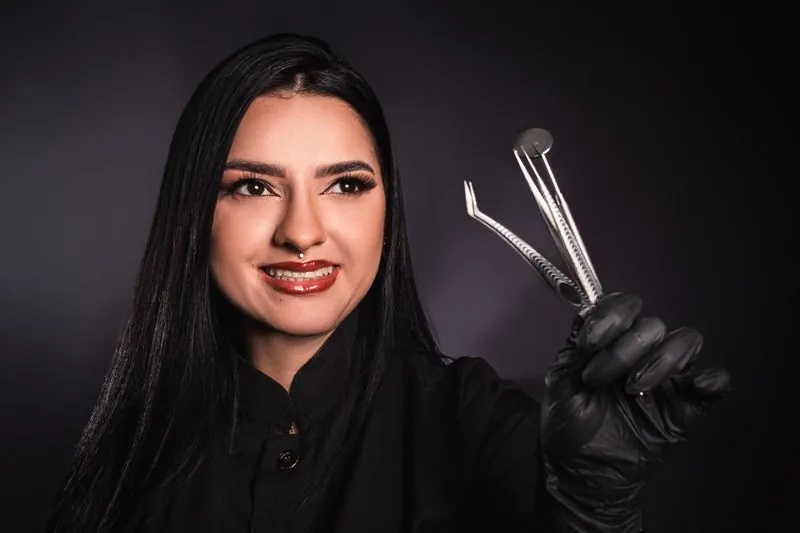 A dentist in black gloves holding instruments against a dark background